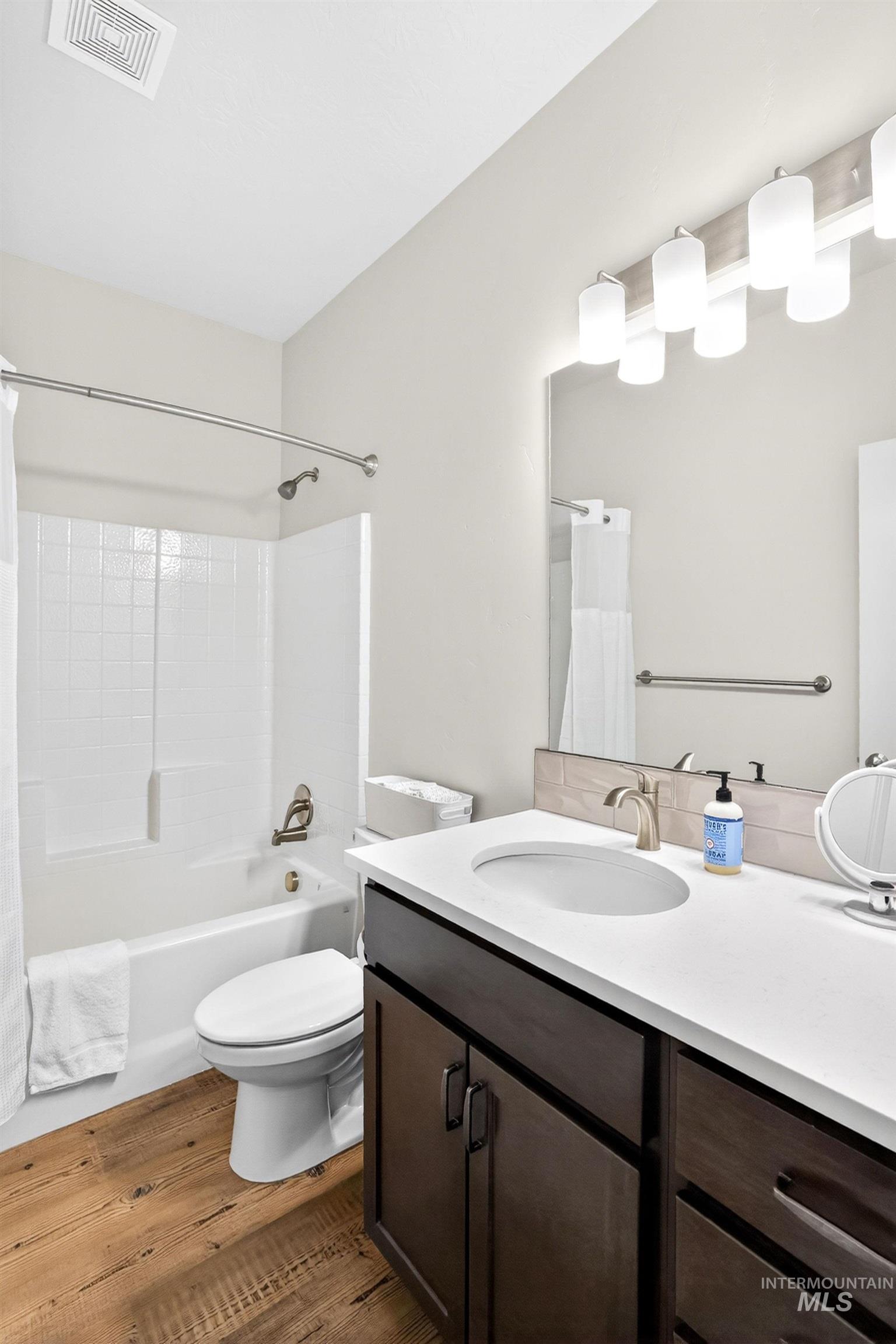 Bathroom featuring a white bathtub with subway tile surround, dark wood-finish vanity with white countertop, and wood-finish flooring