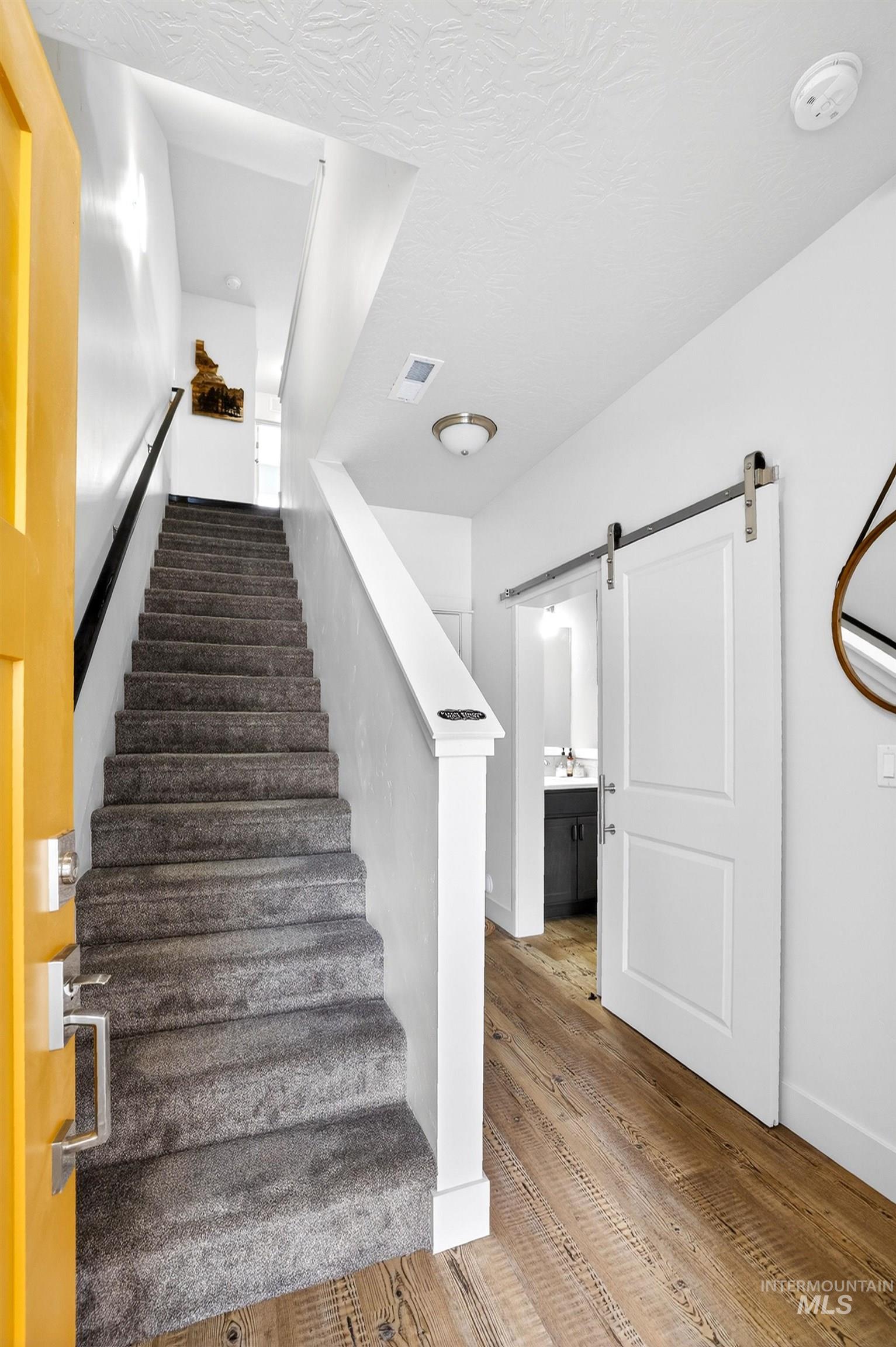 Entryway featuring wood-finish flooring, a carpeted staircase, and a white barn door