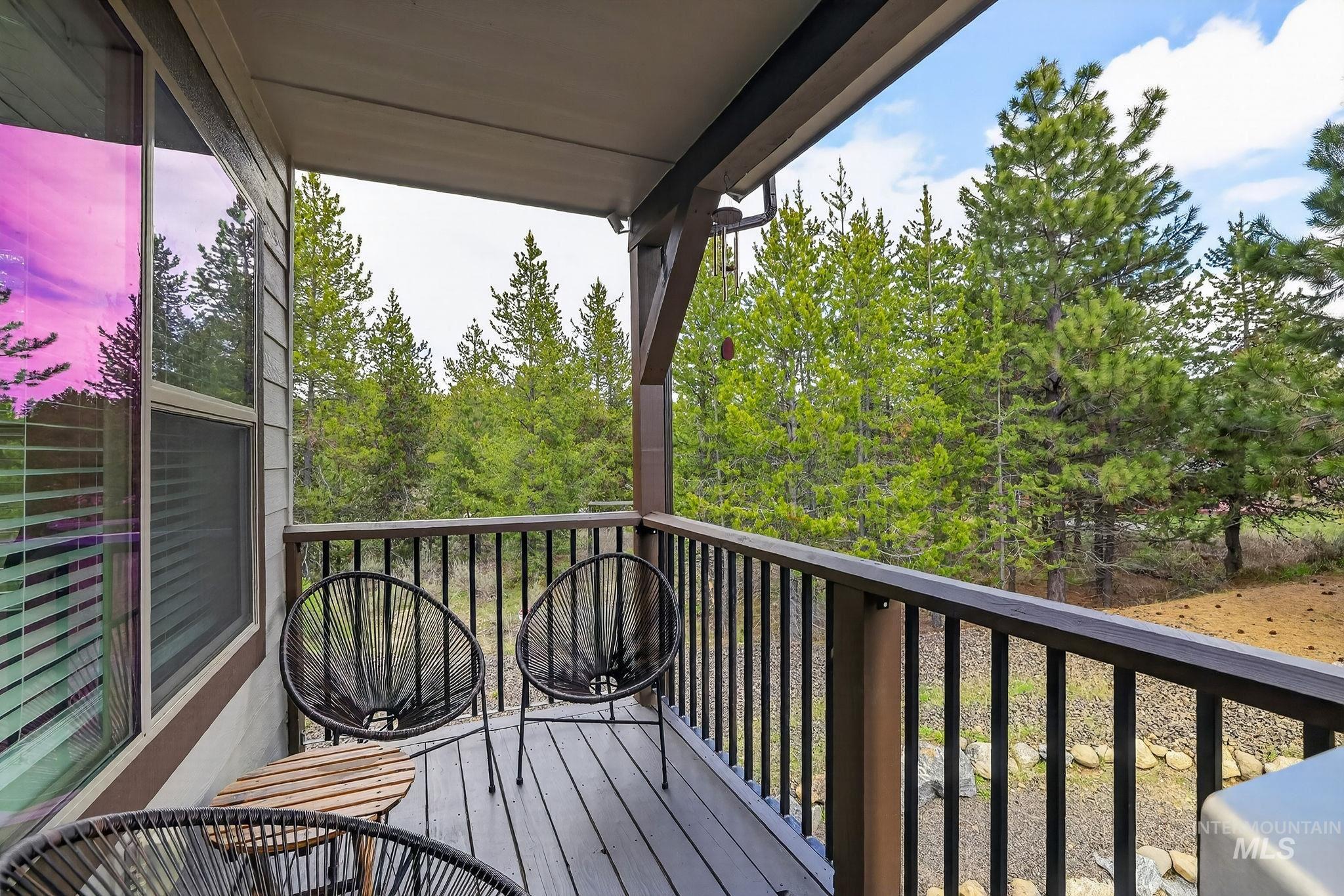 Covered balcony with composite decking, black metal railings, and a backdrop of mature evergreen trees
