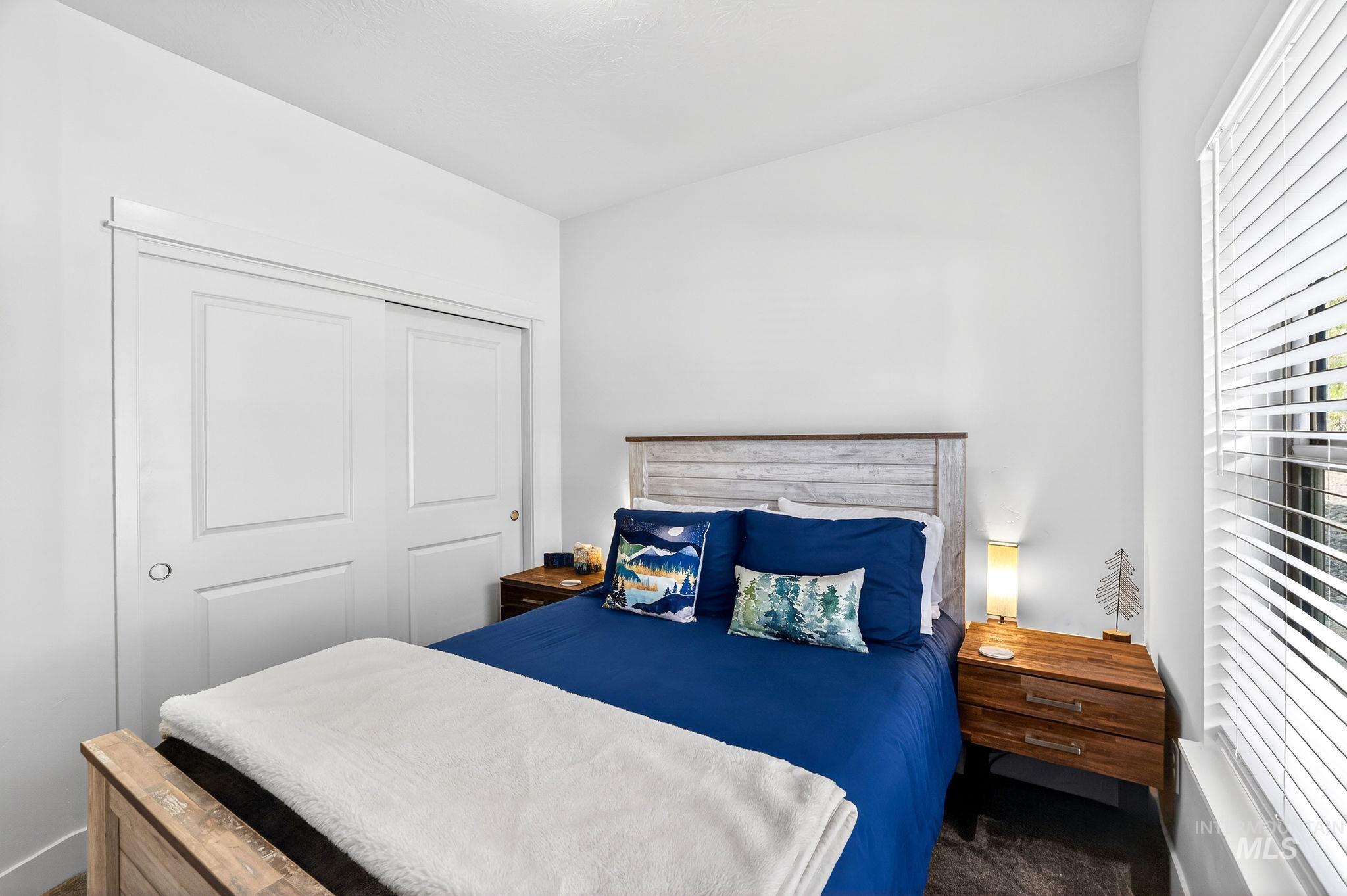 Vaulted ceiling bedroom featuring a wood-finish bed frame with a contrasting headboard, a built-in sliding closet with panel doors, and a window with horizontal blinds