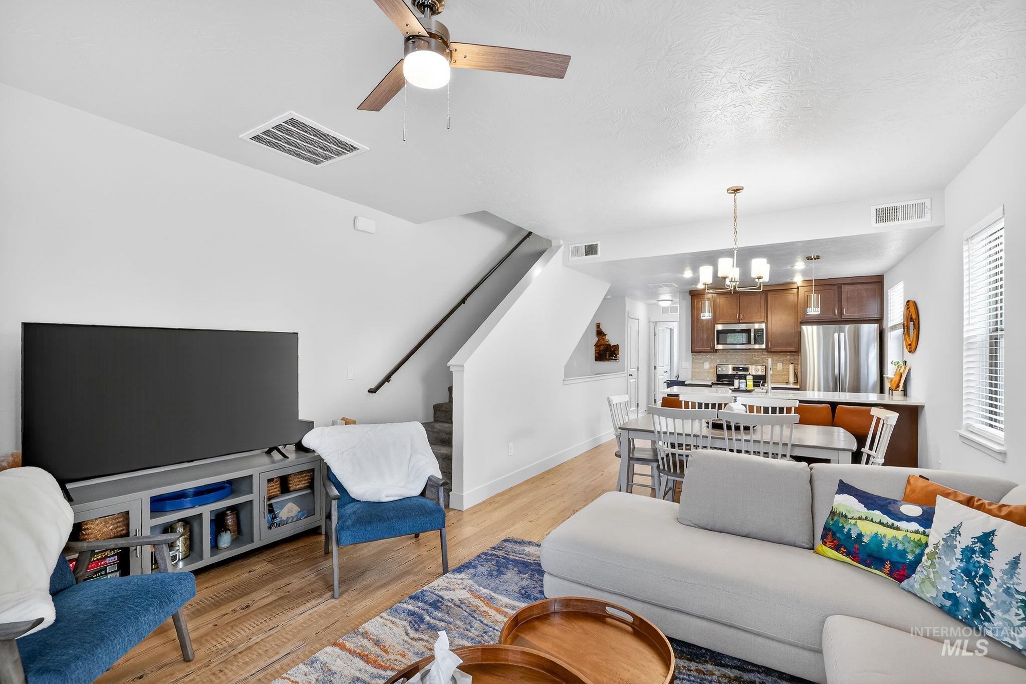 Open-concept living space featuring wood-finish flooring, a ceiling fan, and a staircase with a dark handrail