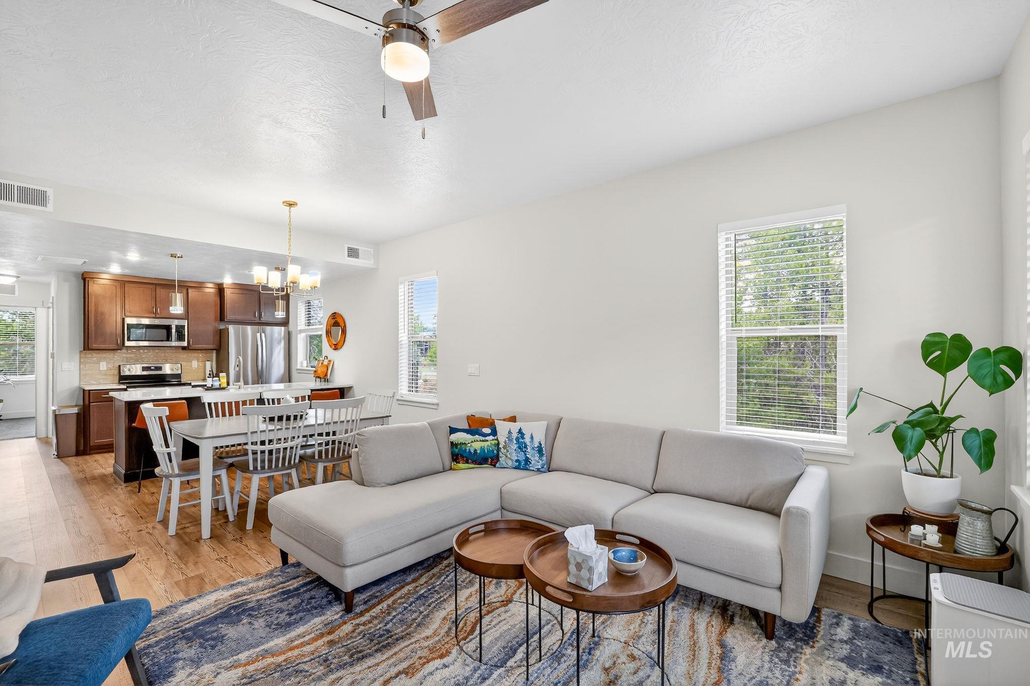 Open-concept living area with wood-finish flooring, a ceiling fan, and multiple windows