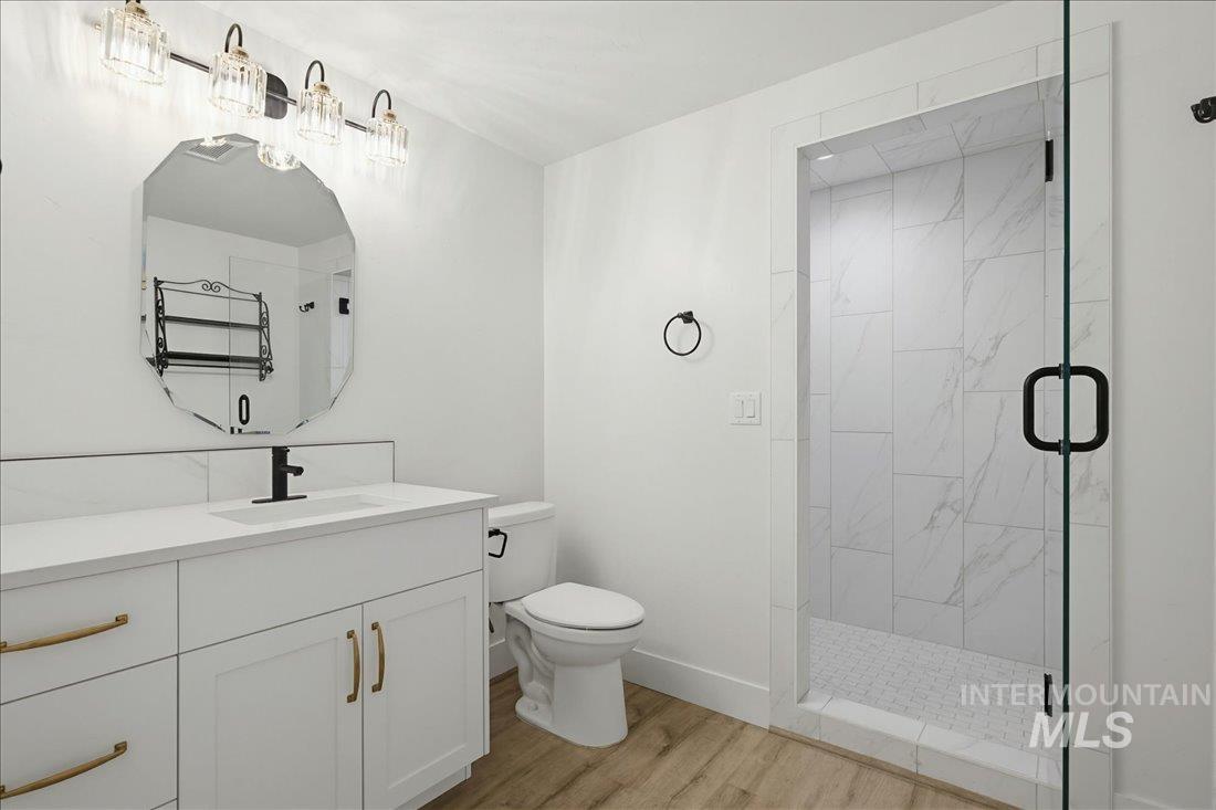 Contemporary bathroom featuring a frameless glass shower enclosure with white marble-look tile, a white vanity with gold-tone hardware and a matte black faucet, a large faceted mirror, and wood-finish flooring
