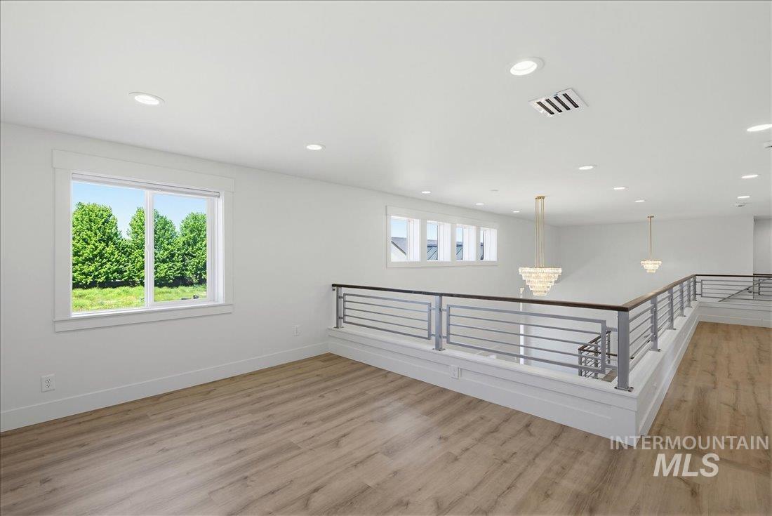 Spacious upper-level area featuring light wood-finish flooring, recessed lighting, and a contemporary horizontal bar railing with a wood cap