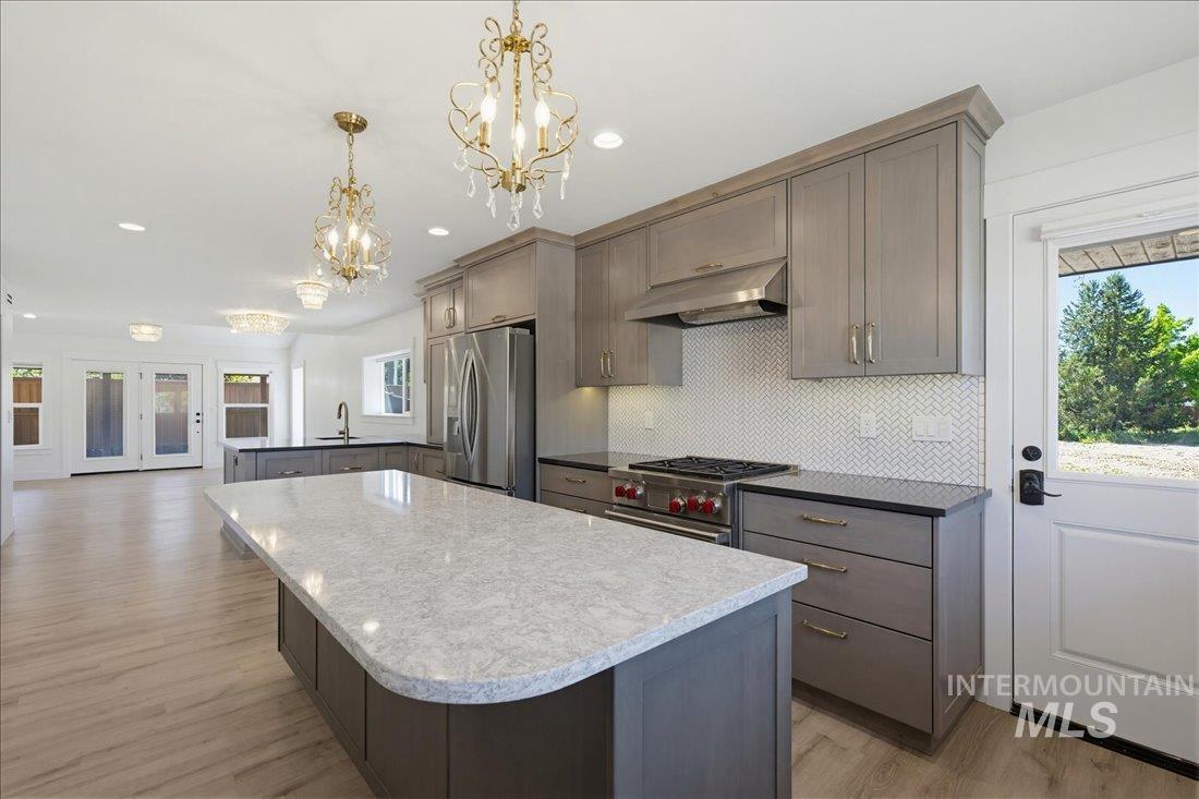 Expansive kitchen featuring an oversized island with a light-toned countertop, gray cabinetry, stainless steel appliances, and wood-finish flooring