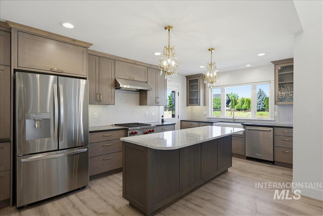 Kitchen featuring stainless steel appliances, wood-finish flooring, a central island with a light-toned countertop, custom cabinetry, and pendant lighting fixtures