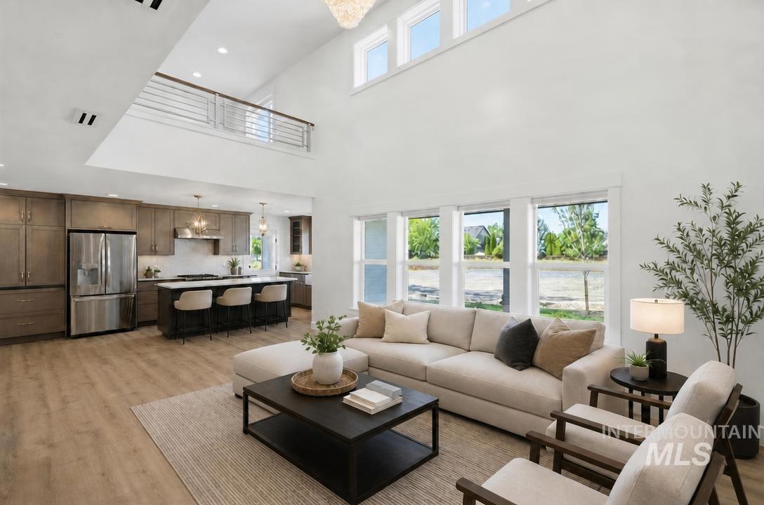 Open-concept living space featuring high ceilings, wood-finish flooring, a kitchen island with seating, stainless steel appliances, and a second-story interior balcony
