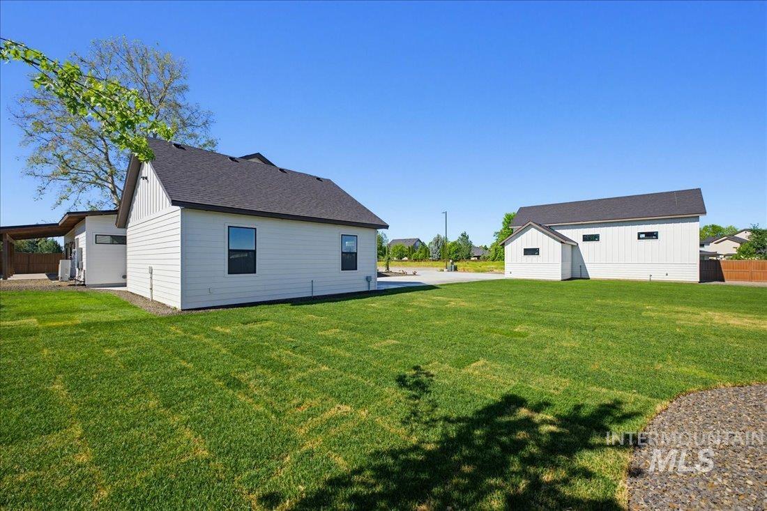 Expansive green lawn with a white siding structure featuring dark trim windows and a dark shingled roof