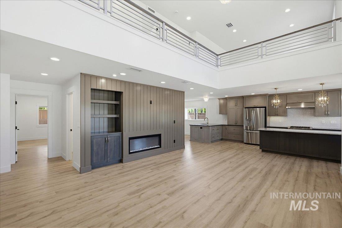 Open-concept interior featuring wood-finish flooring, a contemporary fireplace, and a two-story ceiling with an overhead railing