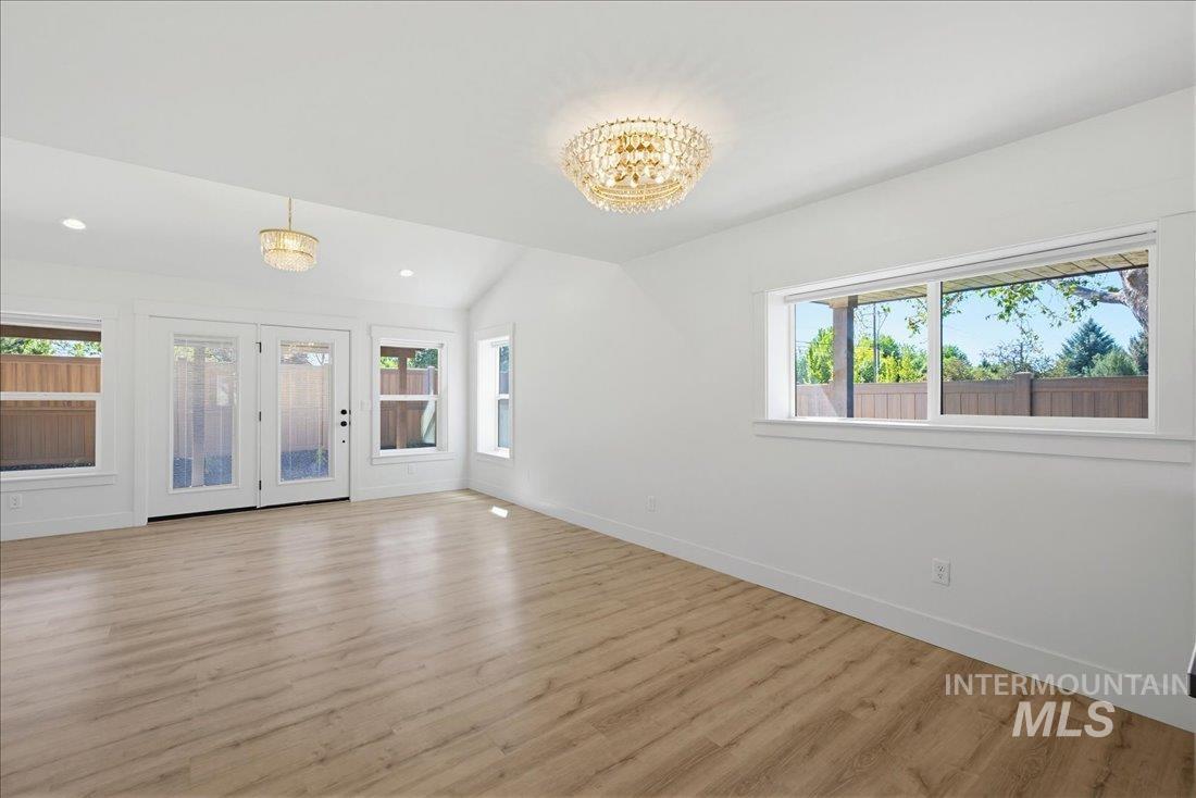 Spacious room featuring wood-finish flooring, crisp white walls, and a vaulted ceiling