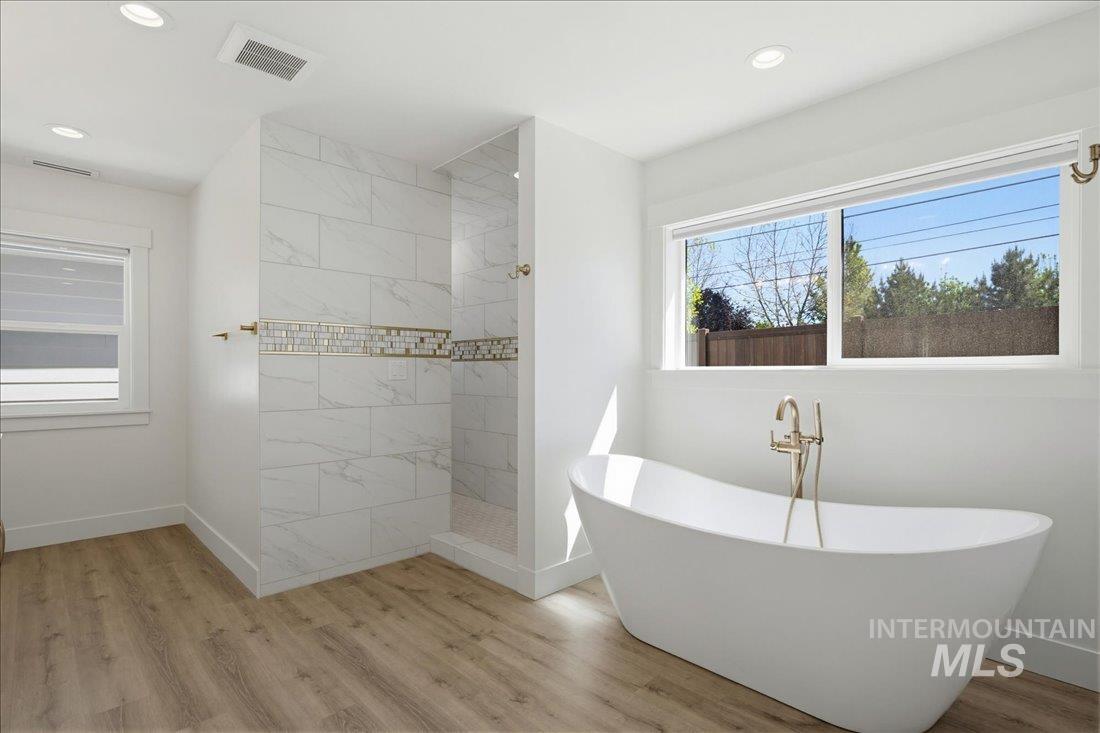 Contemporary bathroom featuring a freestanding soaking tub with a floor-mounted gold-tone faucet, a tiled walk-in shower with mosaic accent band, wood-finish flooring, and recessed ceiling lighting