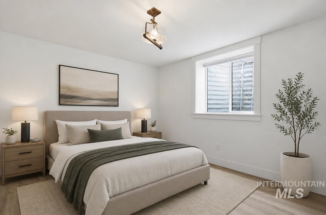 Bright bedroom with a window, contemporary ceiling light fixture, wood-finish flooring, and crisp white walls