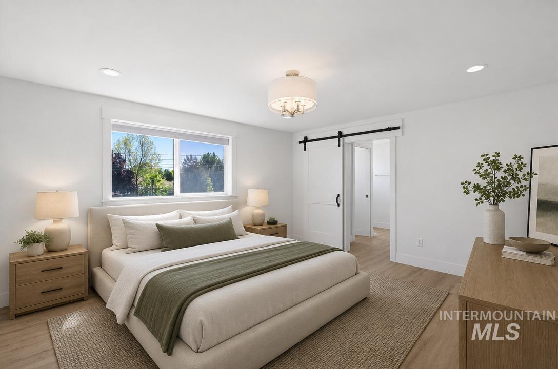 Spacious bedroom featuring light wood-finish flooring, a contemporary ceiling light fixture, recessed lighting, and a white barn door