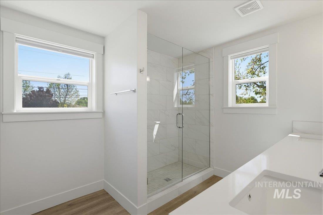 Modern bathroom featuring a glass-enclosed shower with tile surround, a built-in vanity with an integrated sink, two windows, and wood-finish flooring