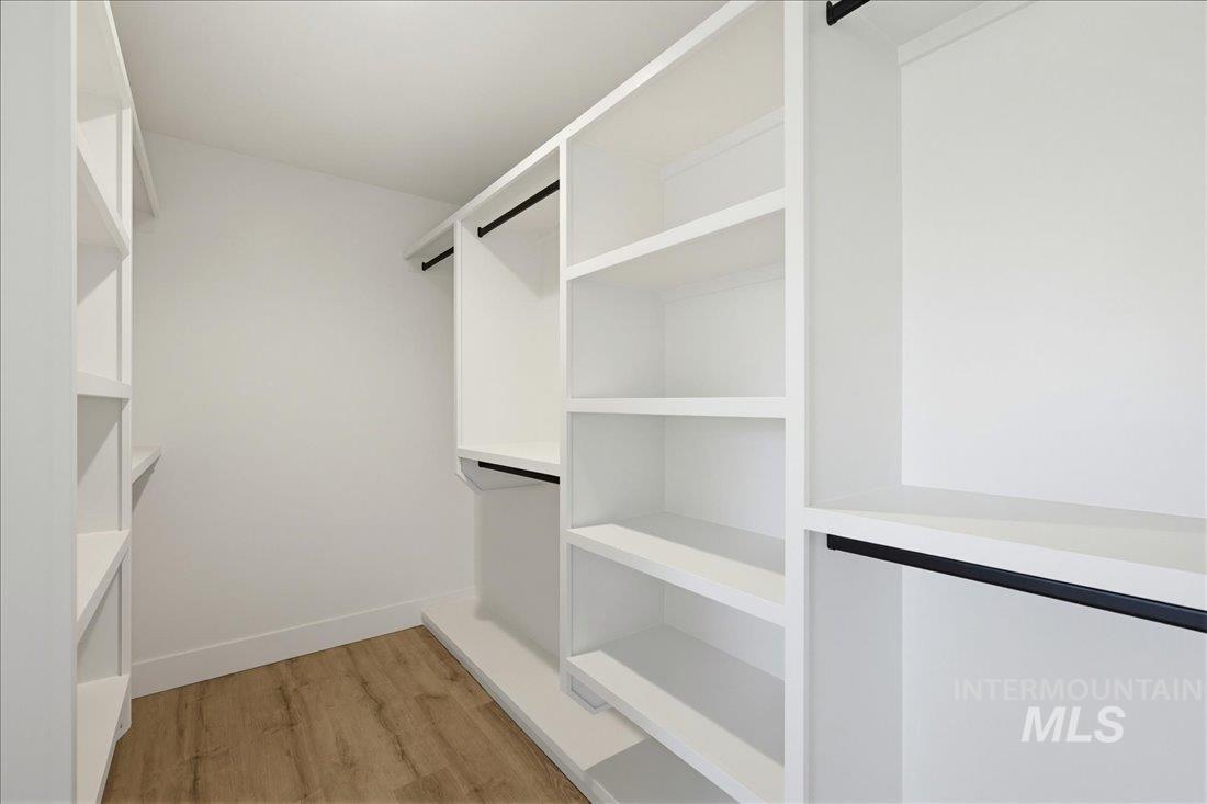 Custom closet system featuring white built-in shelving, hanging rods, and wood-finish flooring