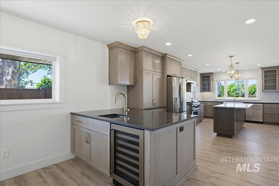 Spacious kitchen featuring two islands with contrasting cabinetry, stainless steel appliances, wood-finish flooring, recessed lighting, and a large window overlooking exterior greenery