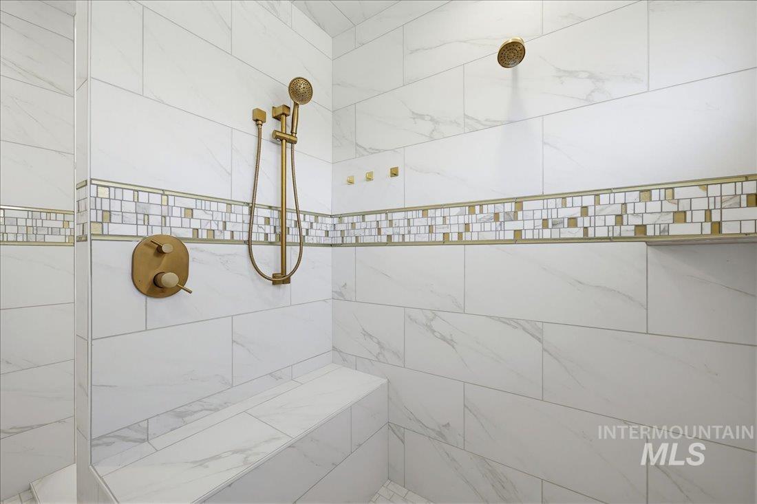 Shower enclosure featuring large format white tile with subtle veining, mosaic accent tile, a built-in bench, and a brushed brass shower system with a handheld sprayer