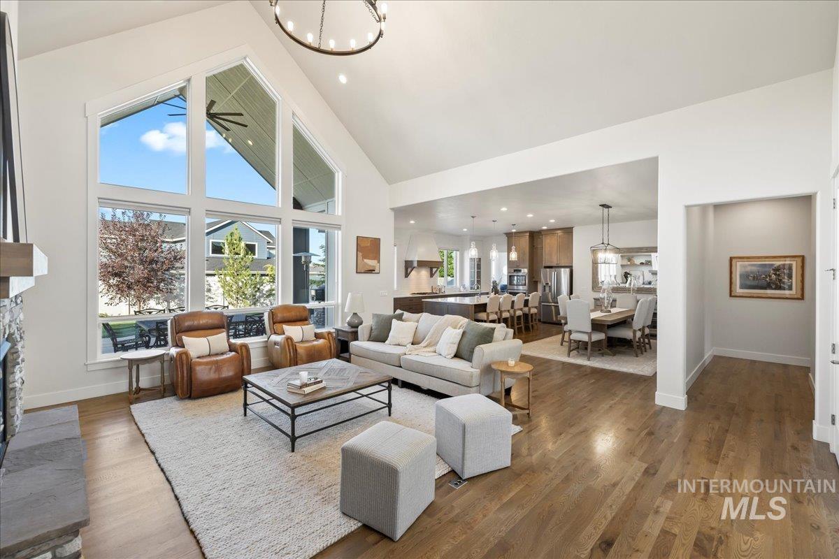 Living room featuring high vaulted ceiling, a chandelier, dark wood finished floors, and a stone fireplace