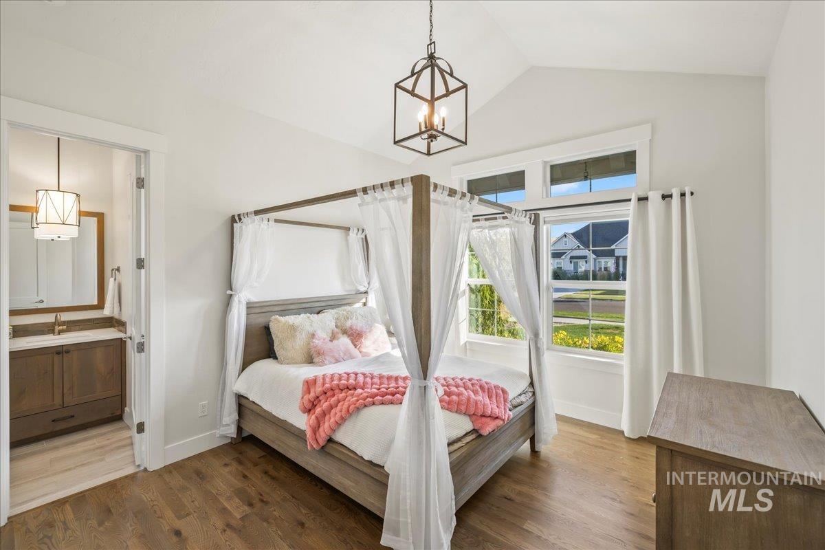 Bedroom featuring lofted ceiling, a chandelier, wood finished floors, and connected bathroom