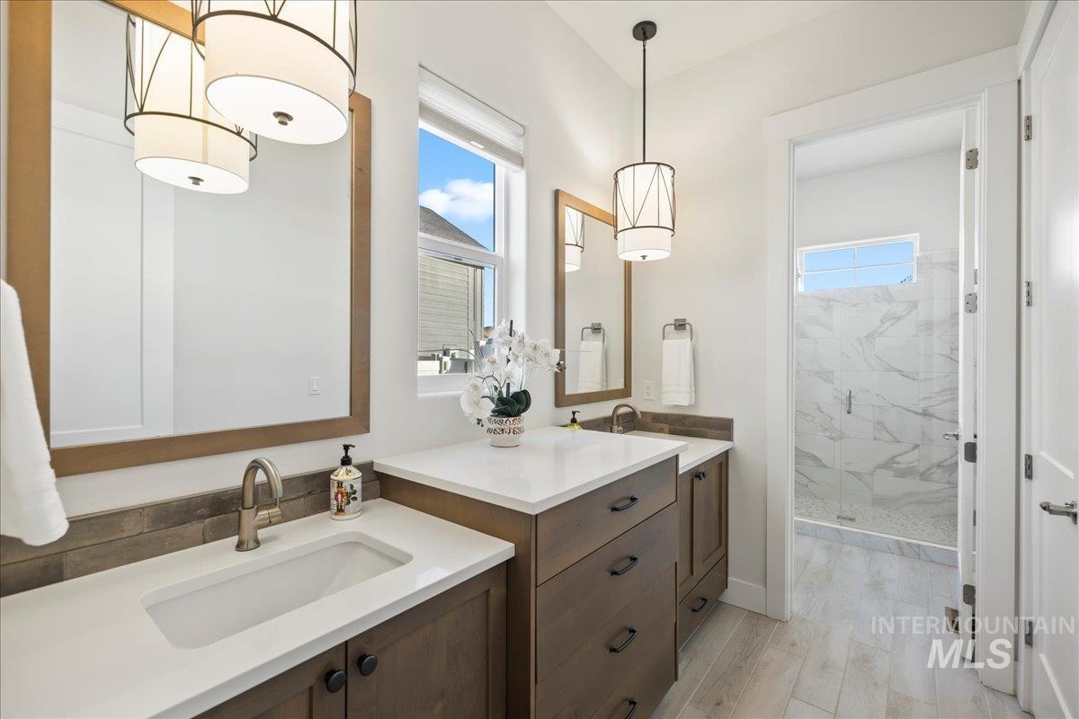 Bathroom with a marble finish shower, two vanities, and wood finished floors
