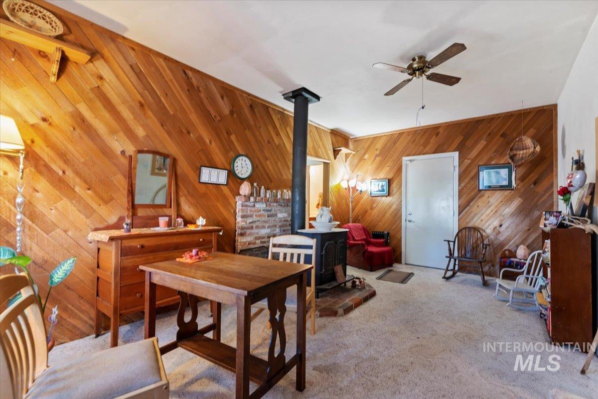 Dining area with a wood stove, carpet floors, ceiling fan, and wood walls
