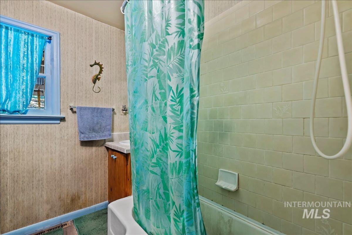 Bathroom featuring wallpapered walls, shower / bathtub combination with curtain, and vanity