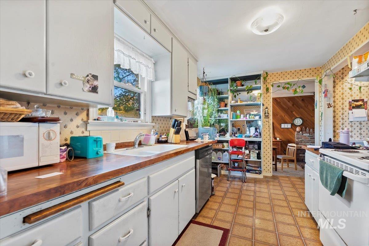 Kitchen featuring white cabinetry, white appliances, tasteful backsplash, butcher block countertops, and wallpapered walls
