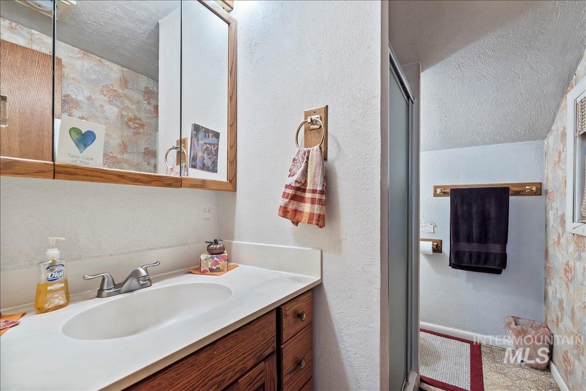 Full bathroom featuring a textured ceiling, vanity, a shower stall, and a textured wall