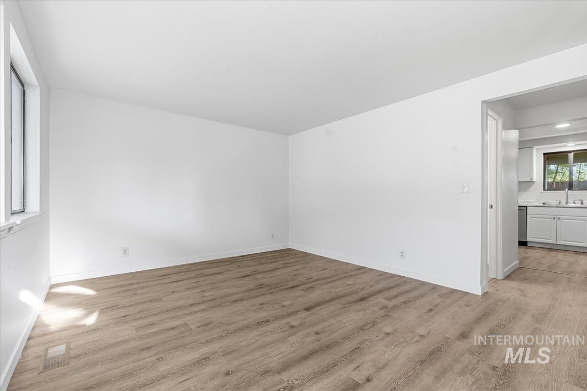 Spacious room featuring wood-finish flooring, white walls, and a large window