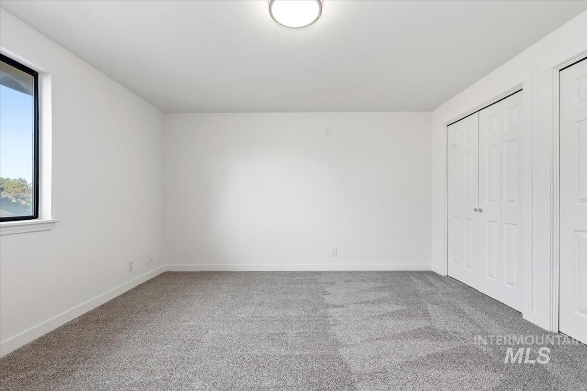 Spacious room featuring neutral carpeting, white walls, a large window with black framing, and two double-door closets