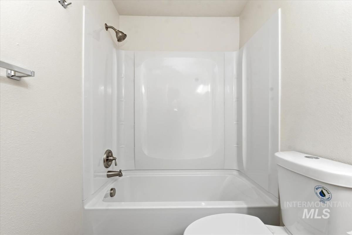 White bathtub with integrated shower, brushed nickel fixtures, and a white toilet