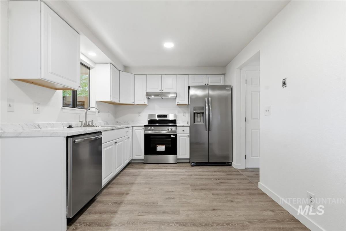 Modern kitchen featuring white cabinetry, stainless steel appliances, wood-finish flooring, recessed lighting, and a window above the sink