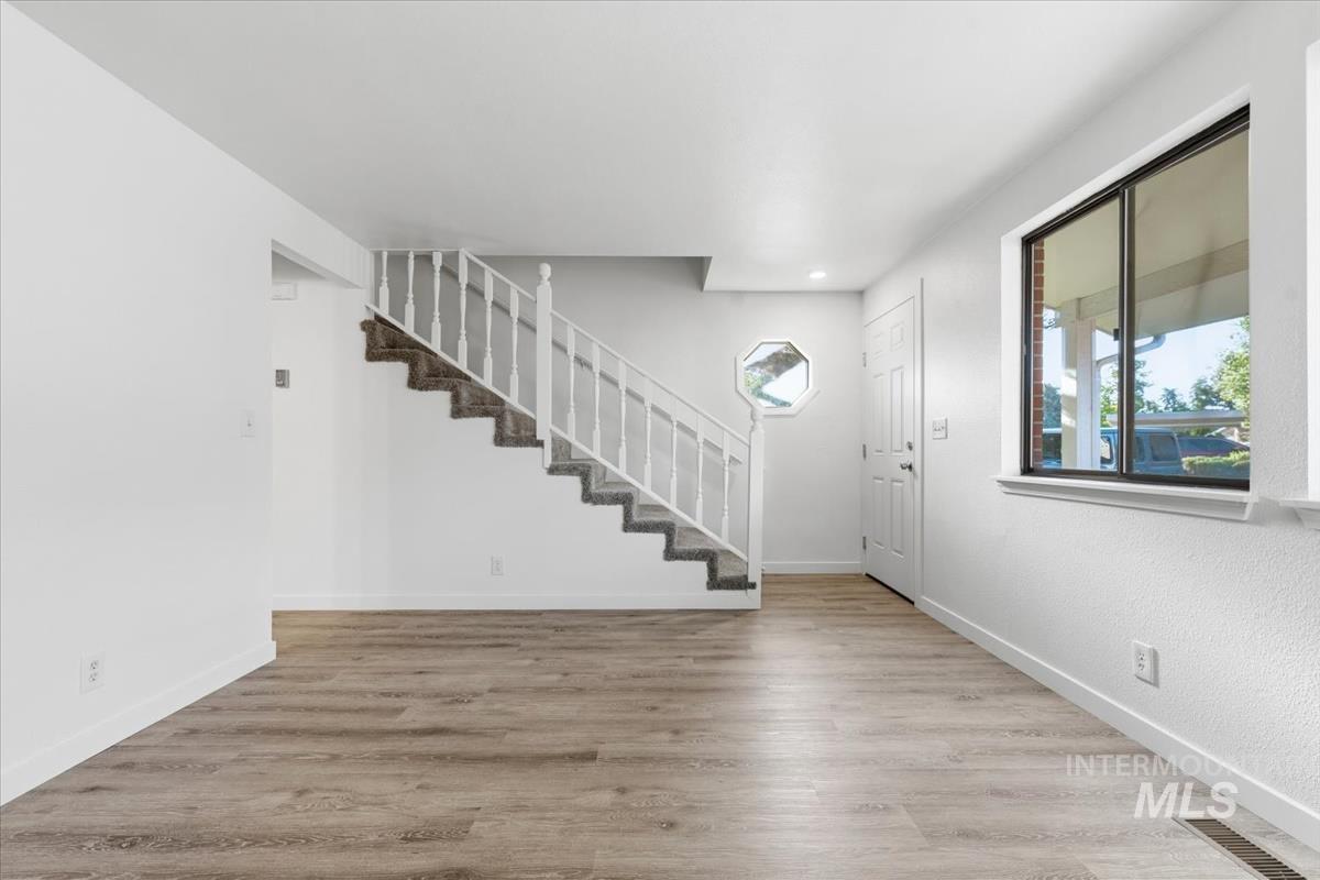 Spacious interior featuring wood-finish flooring, a carpeted staircase with white balusters, a rectangular window with dark trim, a white entry door, and an octagonal window