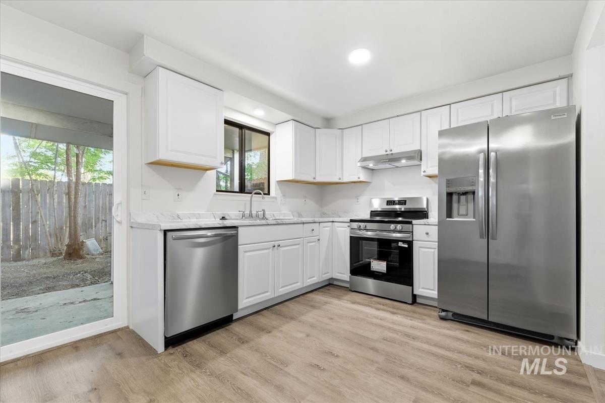 Kitchen with white cabinetry, stainless steel appliances, and wood-finish flooring