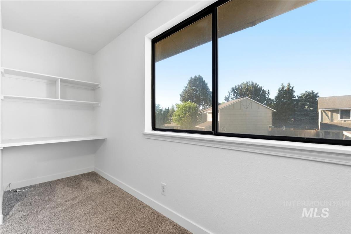 Bright room featuring a large black-framed window, built-in shelving, a built-in desk, and neutral-toned carpeting
