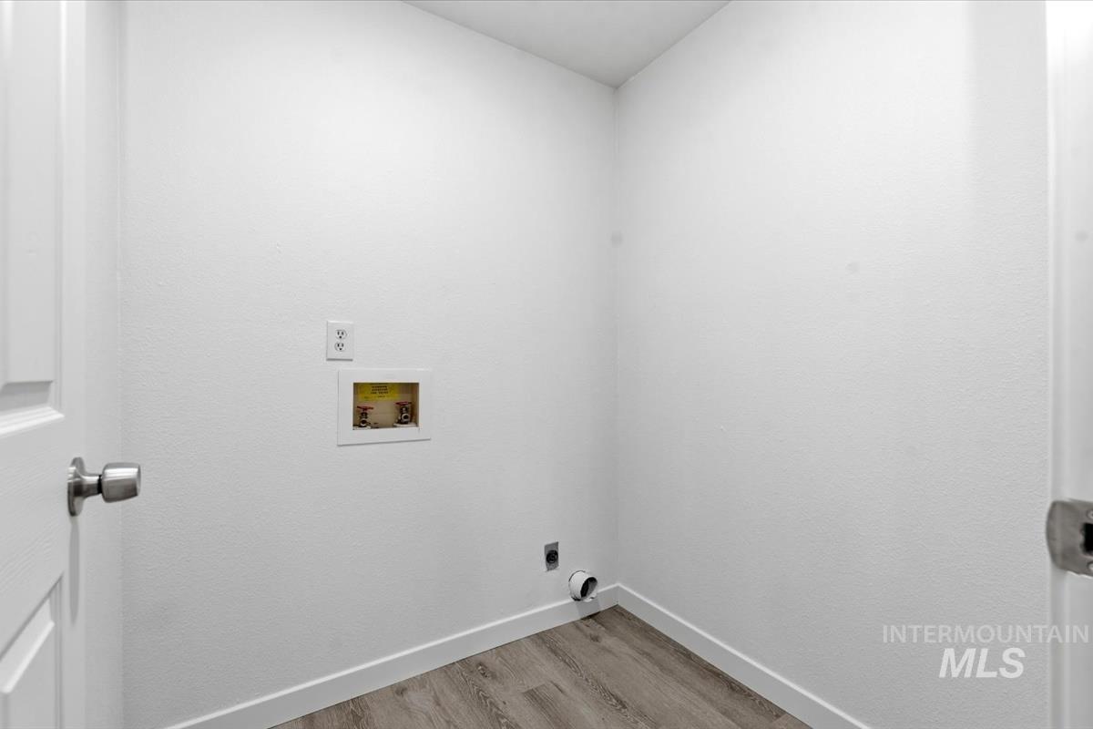 Dedicated laundry area featuring a white paneled door, light wood-finish flooring, white baseboards, and a recessed hook-up for appliances