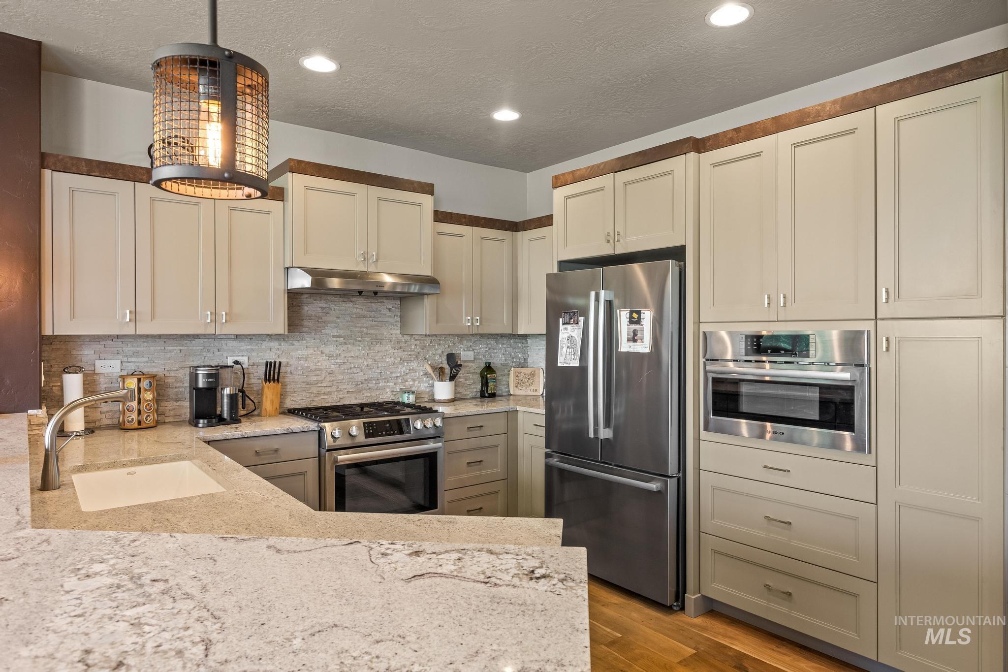 Kitchen with stainless steel appliances, light stone countertops, decorative backsplash, light wood-type flooring, and under cabinet range hood