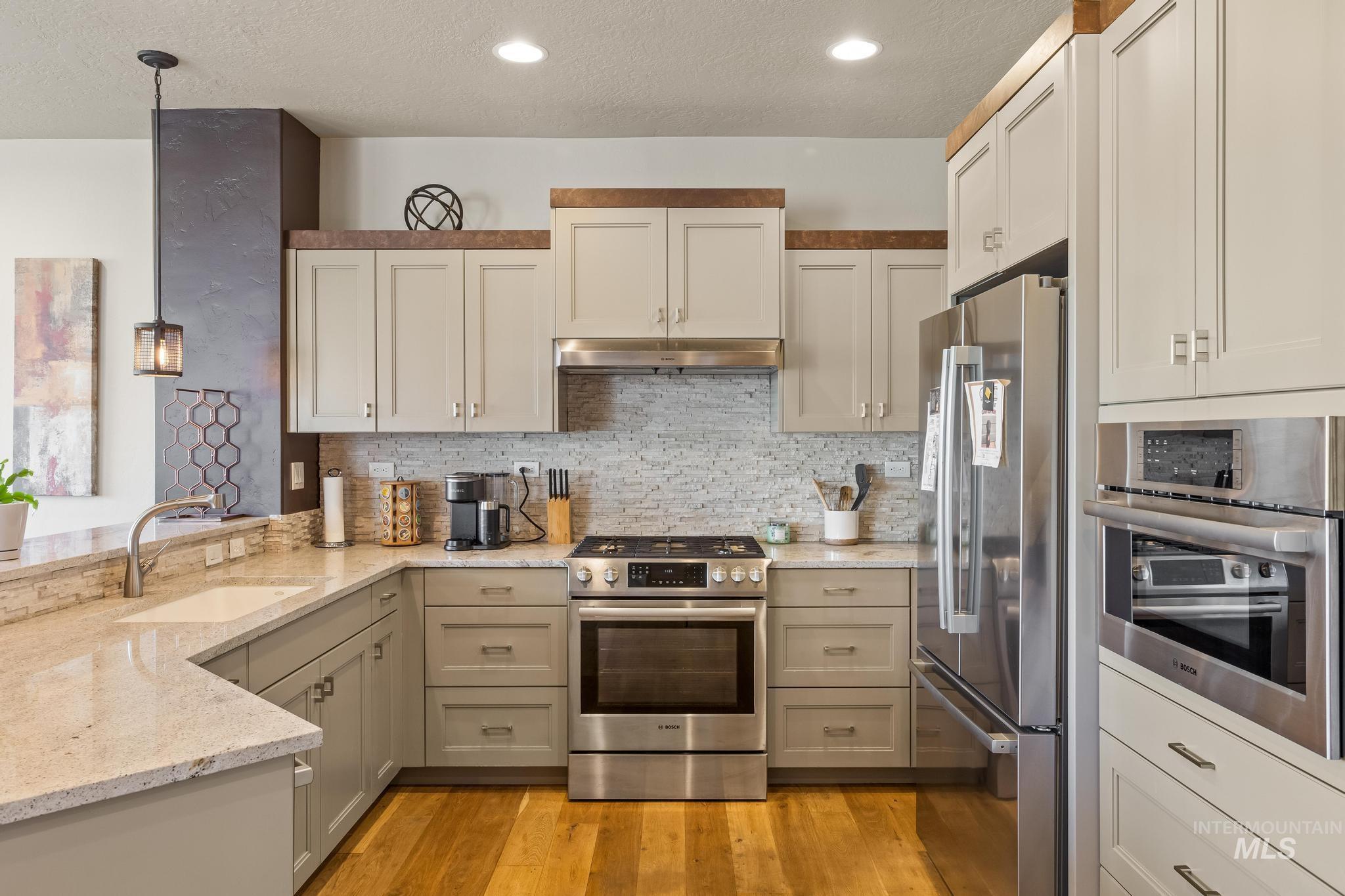 Kitchen with stainless steel appliances, light stone countertops, a textured ceiling, hanging light fixtures, and decorative backsplash