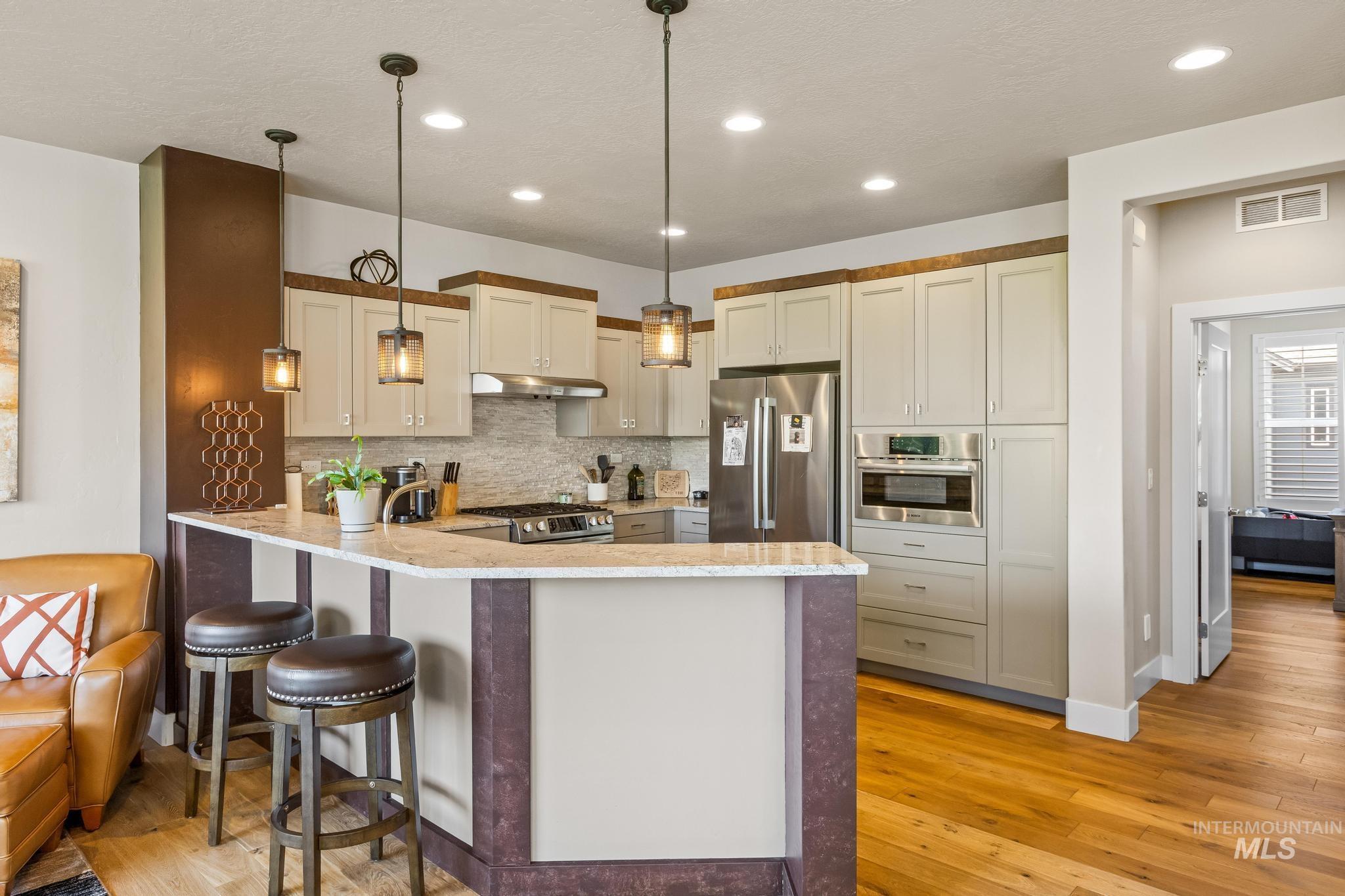 Kitchen with backsplash, stainless steel appliances, a peninsula, pendant lighting, and a breakfast bar