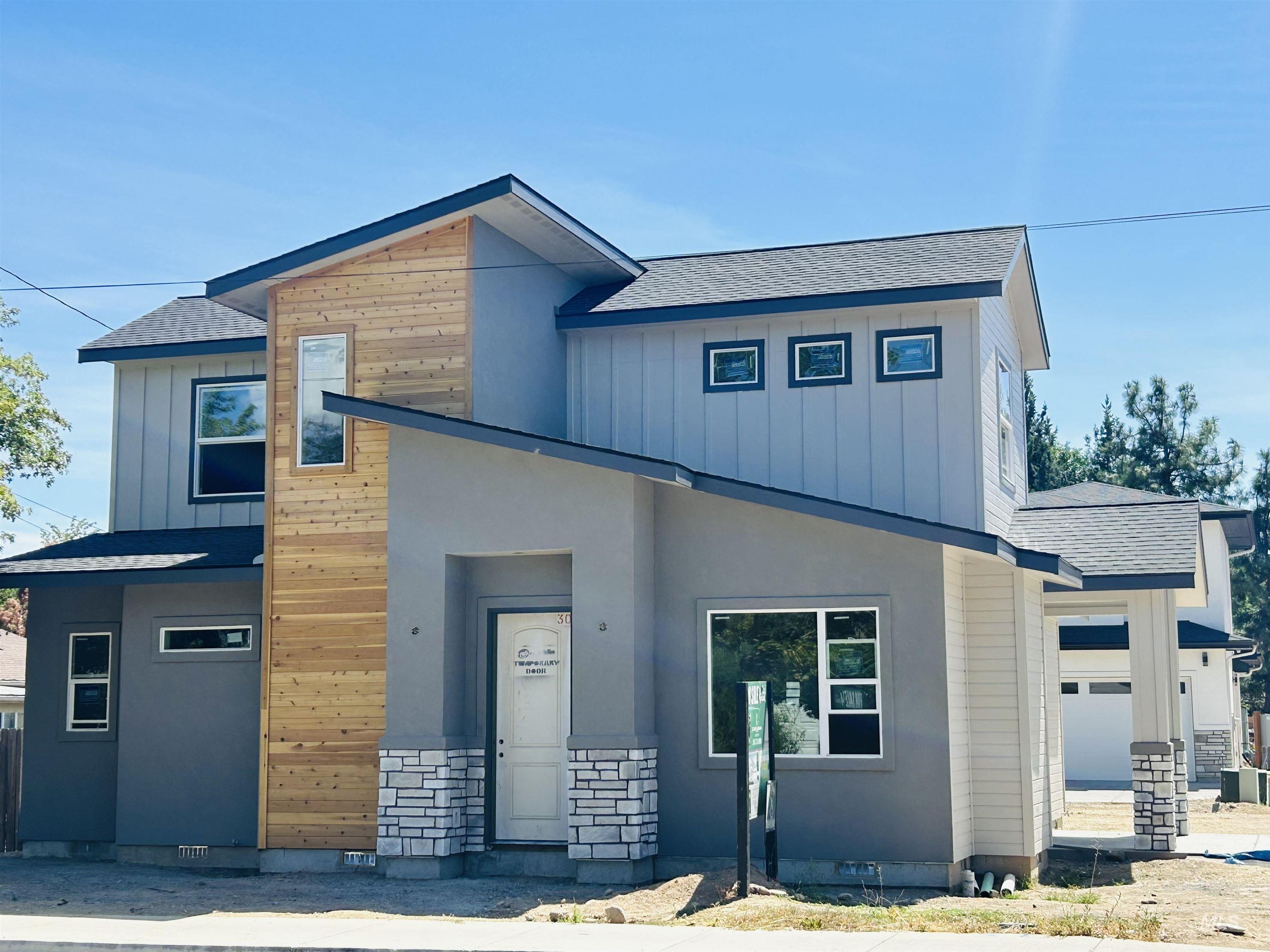 View of front of property featuring roof with shingles, stone siding, a garage, and board and batten siding