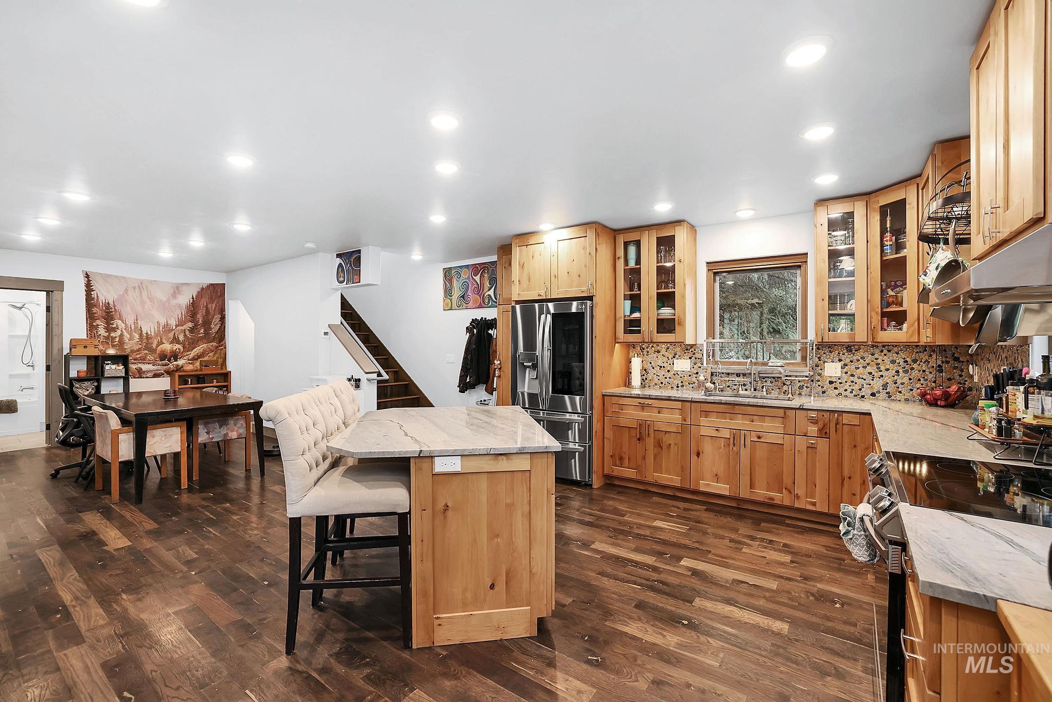 Kitchen featuring light stone counters, appliances with stainless steel finishes, a kitchen breakfast bar, dark wood finished floors, and backsplash