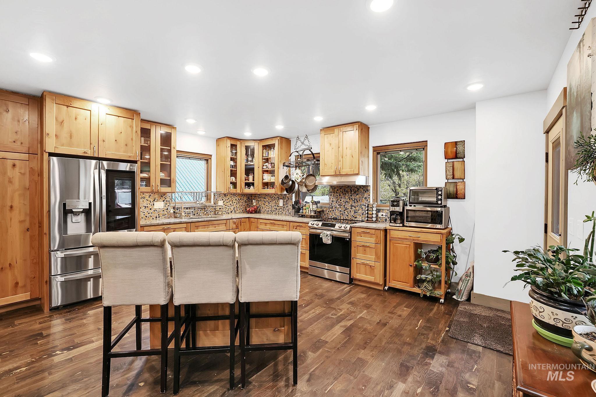 Kitchen with stainless steel appliances, glass insert cabinets, dark wood-type flooring, a kitchen bar, and recessed lighting
