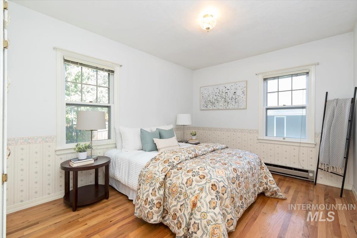 Bedroom featuring wood finished floors, a baseboard radiator, and wallpapered walls