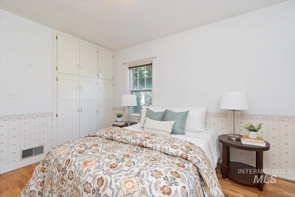 Bedroom featuring wallpapered walls, light wood finished floors, a wainscoted wall, and a closet