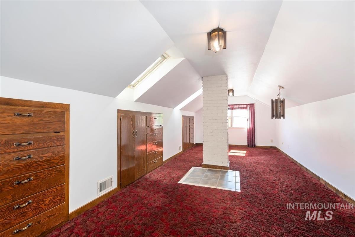 Additional living space with dark carpet and vaulted ceiling
