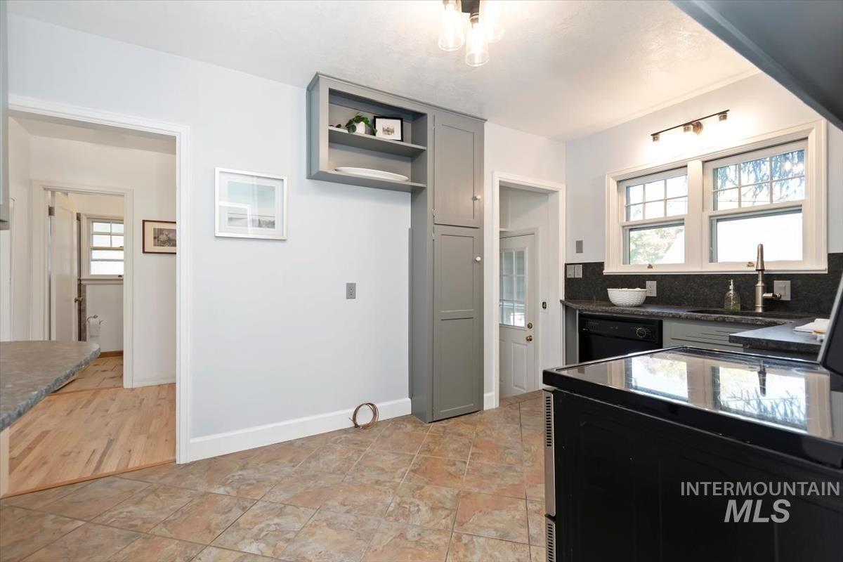 Kitchen with black dishwasher, decorative backsplash, dark stone countertops, and open shelves