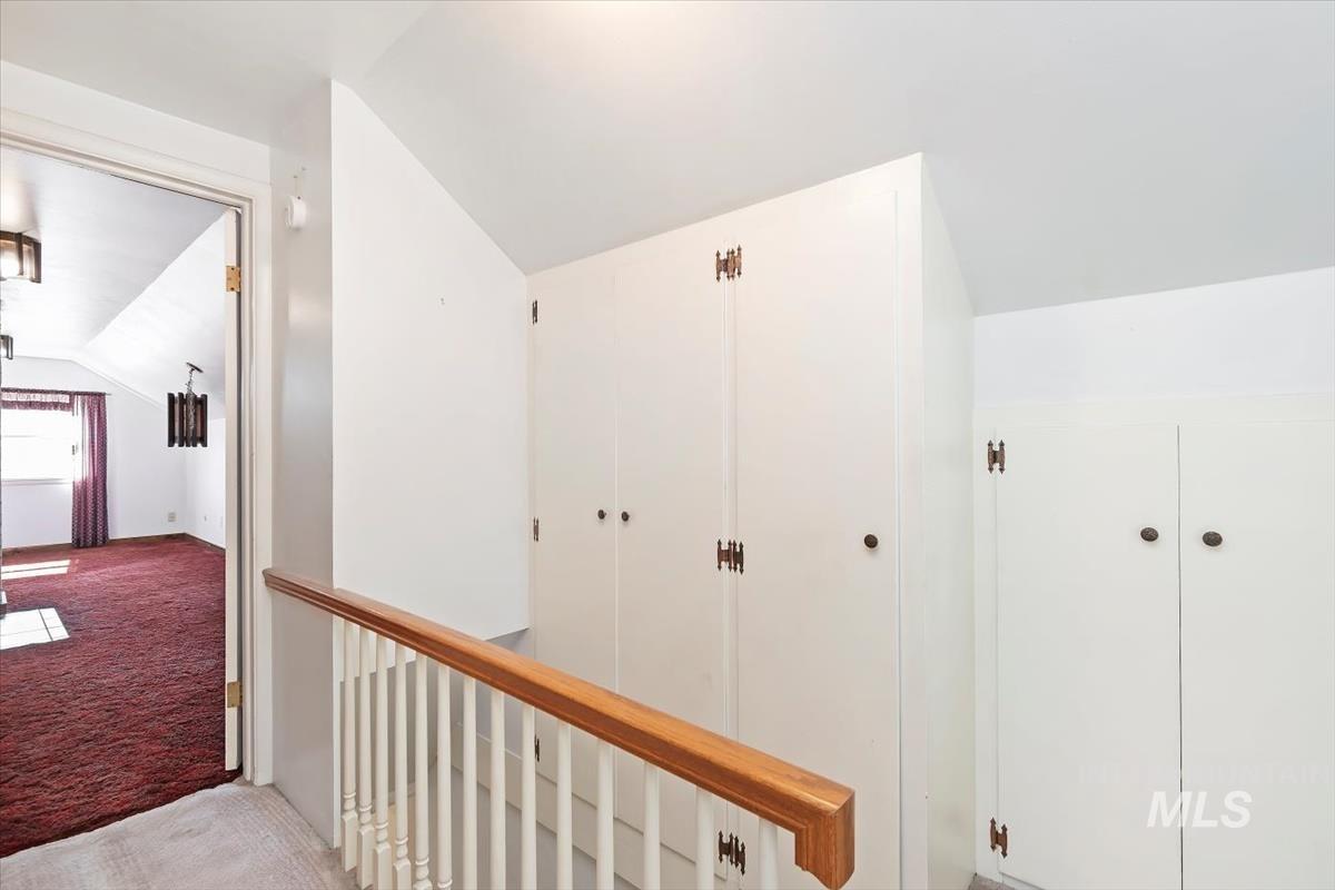 Hallway featuring vaulted ceiling, carpet floors, and an upstairs landing, with storage