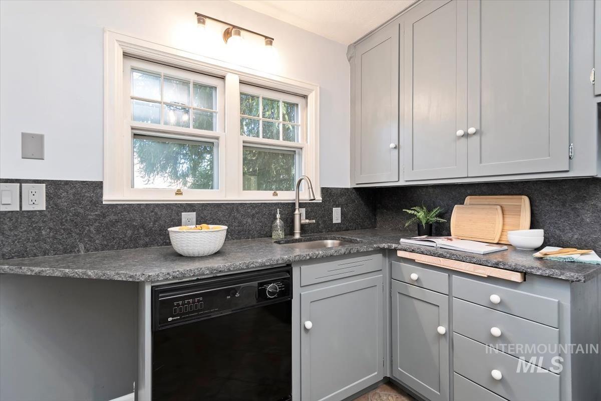 Kitchen with gray cabinets, black dishwasher, and backsplash