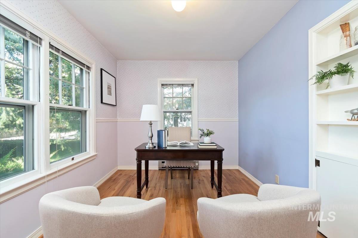 Office space featuring light wood finished floors, wallpapered walls, built in shelves, and a baseboard radiator