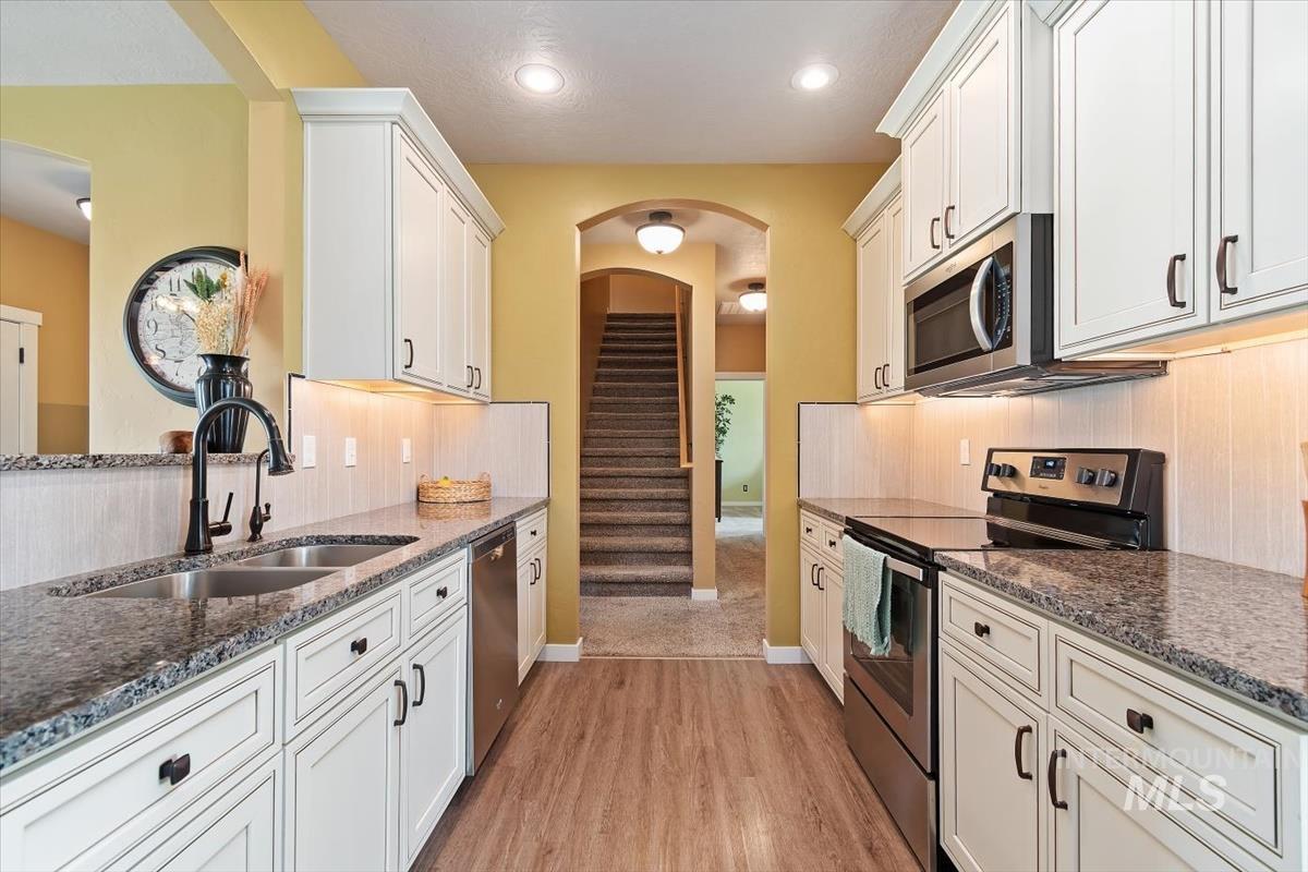 Kitchen with stainless steel appliances, light wood-type flooring, dark stone countertops, white cabinets, and recessed lighting
